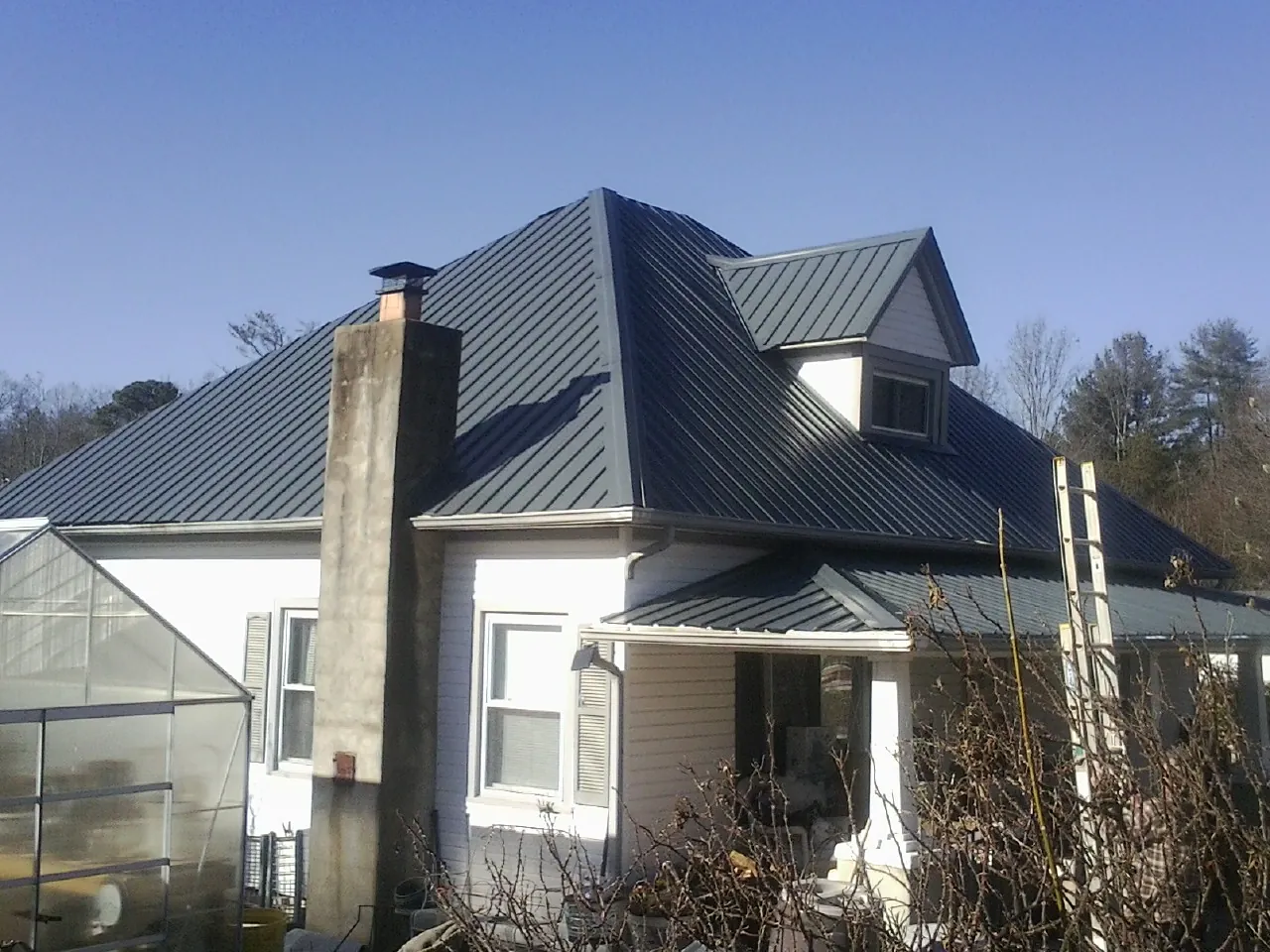 Dark blue standing seam metal roof on a white farmhouse with dormer — Slate & Tile Roof Repair by Roofing Brothers in Bonita