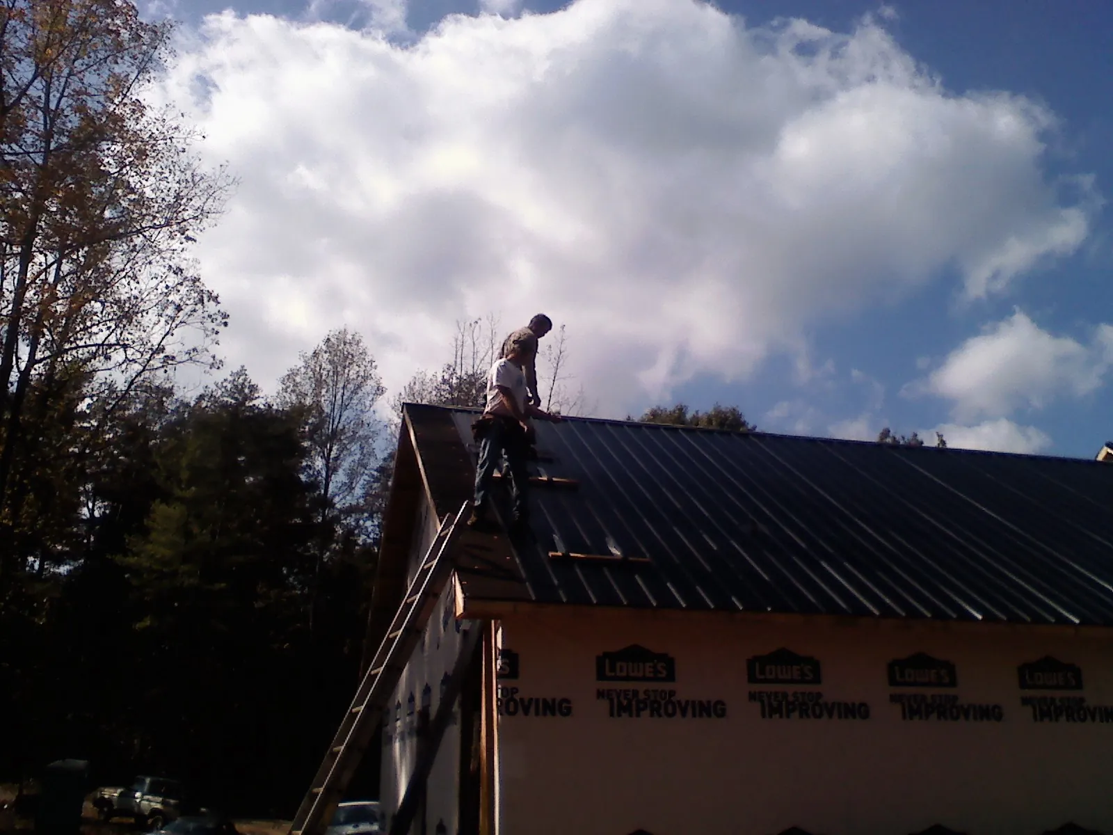 Roofer fastening dark metal panels high against a cloudy sky, from a Roof Inspection job in Bonita