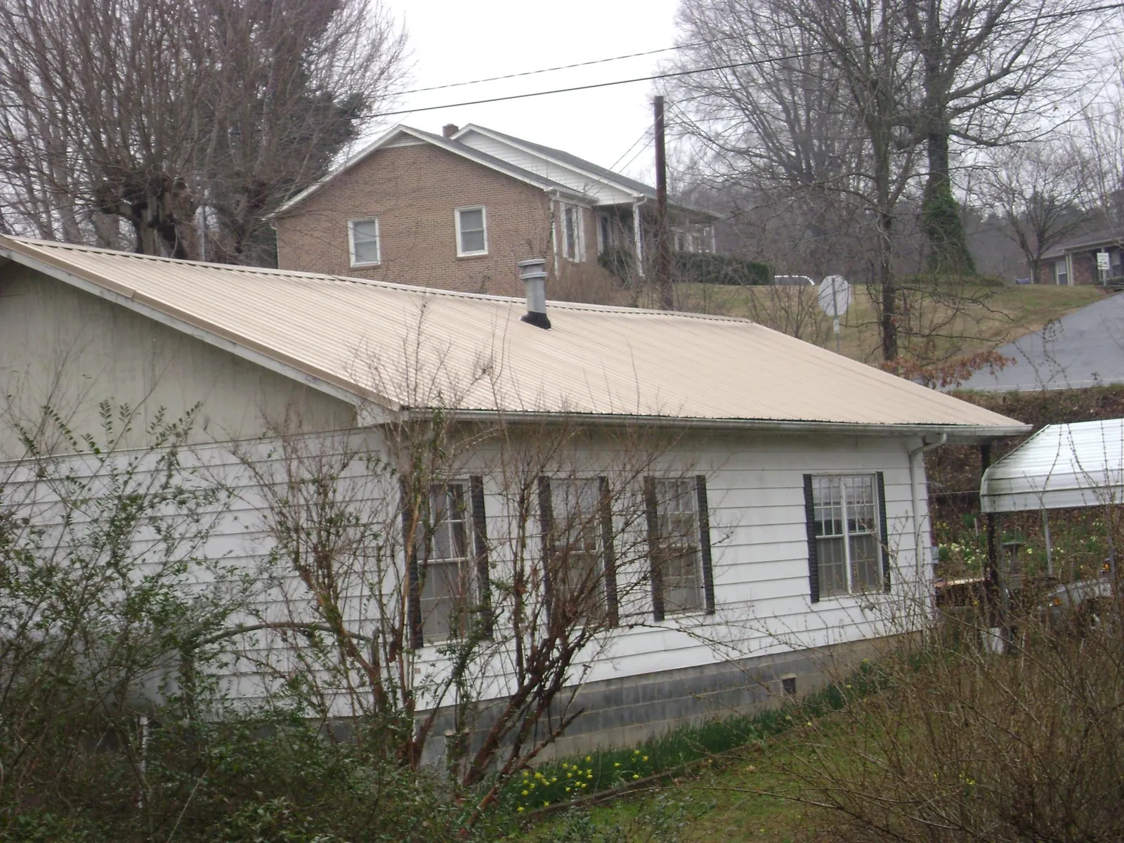 Tan metal roof on a white sided house set into a hillside — Commercial Roofing by Roofing Brothers in Bonita